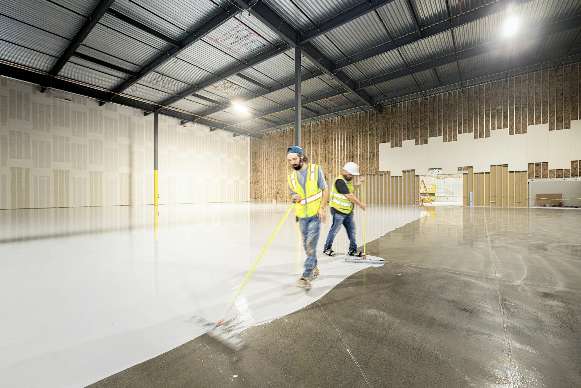 Crew cleaning a large concrete floor inside a new warehouse